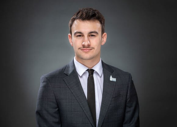 Jacob Iby softly smiles in a suit and tie for a headshot.
