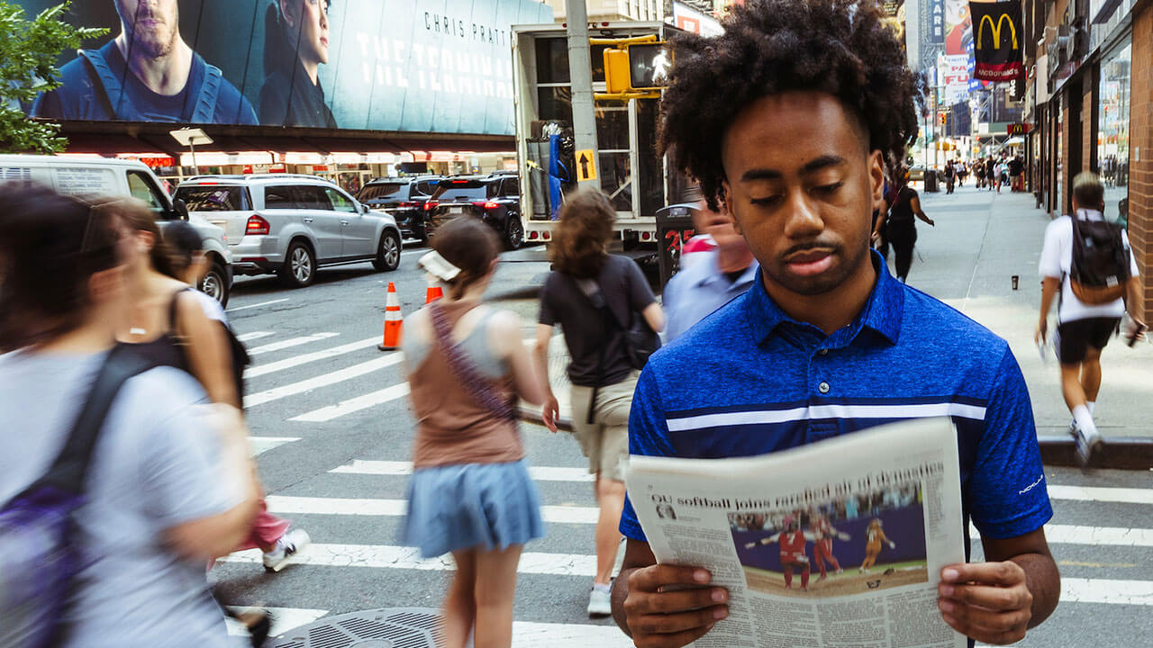 Toyloy Brown pauses to read a magazine on the sidewalk of a bustling city street