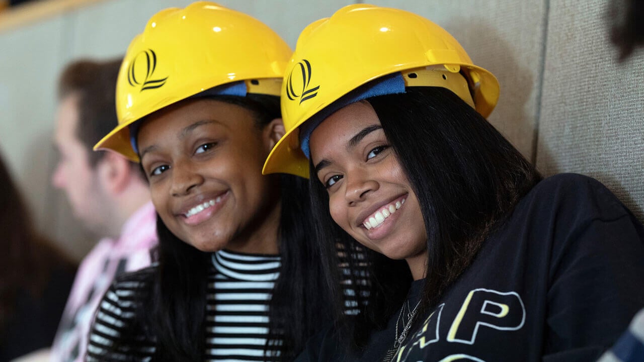 Two students smile while wearing Quinnipiac-branded hard hats