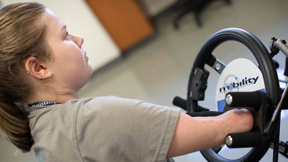 A teenager with limb loss uses a specially-designed steering wheel